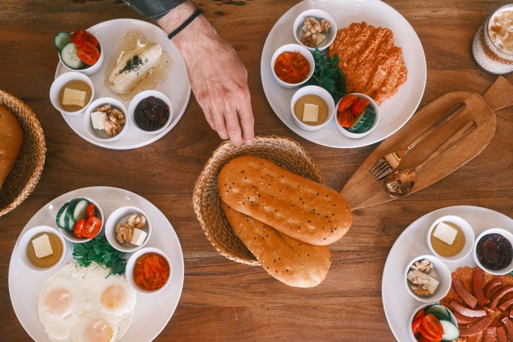 A hand reaching for fresh bread across a table full of shared plates at Hayaat